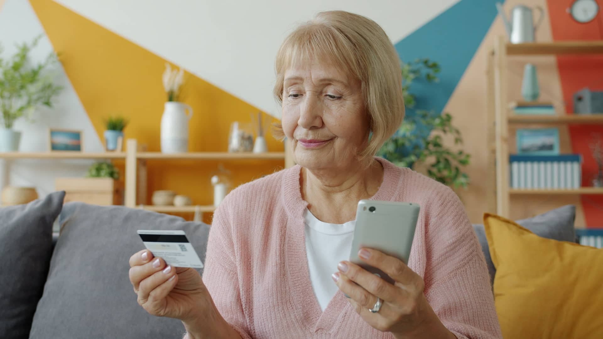 Ältere Frau mit Smartphone und e-card auf dem Sofa